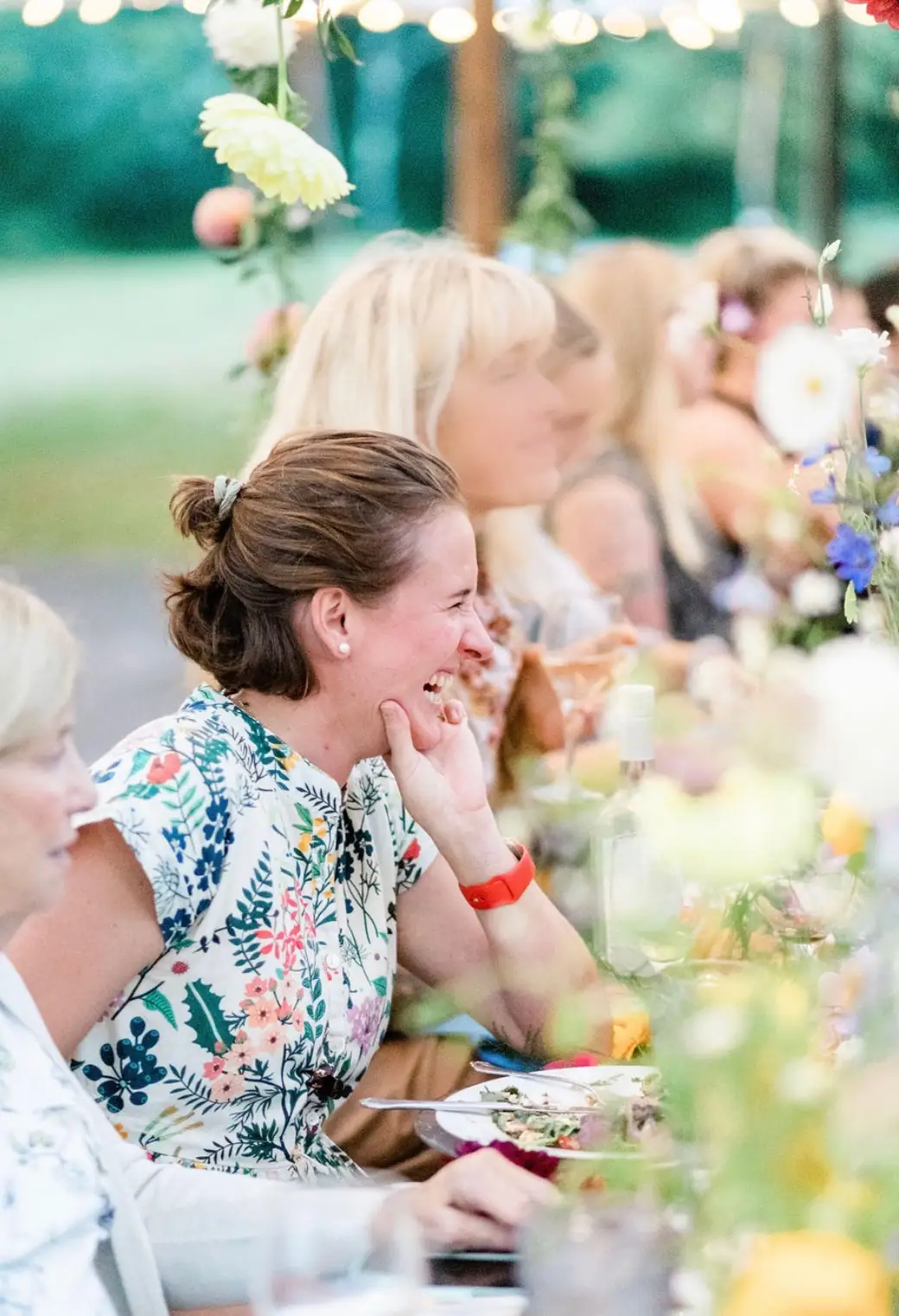 Alba laughing with guests at a long table set with flowers
