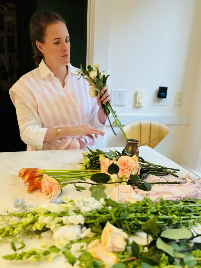 Alba in a striped apron arranging roses at a marble counter