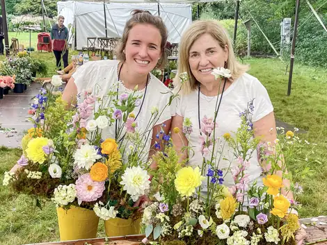 Alba and a guest behind their arrangements at an outdoor workshop