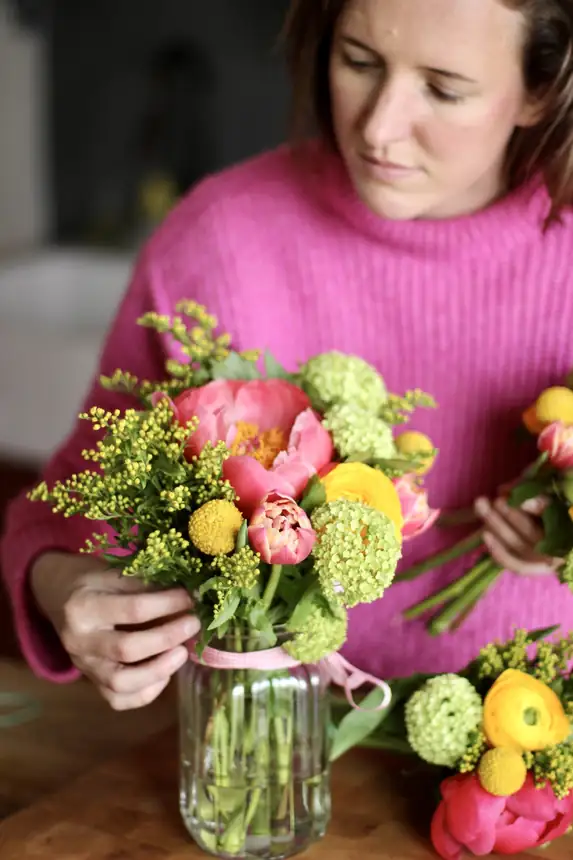 Alba arranging flowers in a jar at a kitchen table